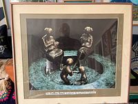 Framed lithograph art showing the full image of bronze sculpture figures on a curved bench with surrounding textured surface.