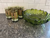 Six green tinted glasses with metallic decoration and a large green glass bowl on countertop