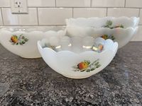 Four white scalloped milk glass bowls with fruit designs grouped on countertop