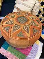 Full view of round Turkish leather ottoman showing leather surface and embroidered patterns
