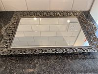 Full view of the rectangular vanity mirror with intricate floral decorative frame placed face up on marble surface.