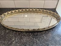 Full view of vintage oval mirror with ornate metal frame laying flat on dark counter