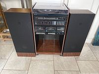 Full view of stereo system main unit with two speakers on either side, wood finish cabinet and black speaker cloth.