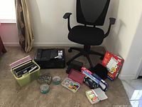 Office chair with black mesh back, file organizer with folders, tubs of staples and paperclips, pens, tape, and other office supplies on carpet.