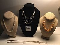 Three necklaces displayed on bust forms and four necklaces laid flat, showing varied styles including pearl and floral designs.