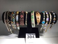 Front view of 12 assorted costume jewelry bracelets on black display stand, showing various designs including chains, enamel, and rhinestones in multiple colors.