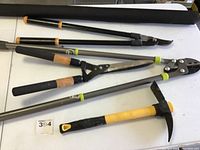 Full set of garden cutting tools and pick axe shown on white table