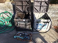 Photo showing two hose reels, one black and one beige, each with a garden hose attached, and a box with hose accessories in front.