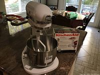 Tilt-head stand mixer assembled with bowl and flat beater on countertop, boxed grinder visible behind