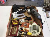 Photo of lot contents including Craftsman staple gun, Porter Cable angle grinder, boxed staples, clamps, Black & Decker tool, and various hardware pieces