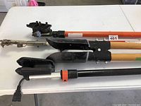 Photo showing multiple pruning tools and tree limb cutters laid on a white table, focusing on cutting heads and handles