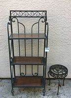 Full view of bakers rack with three wood shelves and adjacent small metal plant stand with scrollwork frame.