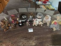 Seven soft animal plush toys in individual clear display boxes on a countertop