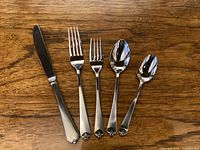 Five key flatware pieces laid out on wooden surface including knife, two forks, soup spoon and teaspoon showing the pattern and style.