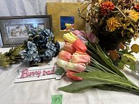 Photo showing artificial flowers including pink and yellow tulips, blue ruffled flowers, a Bunny Trail wooden sign, and framed decorative wall hangings.