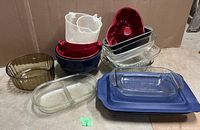 Photo showing assorted baking dishes and mixing bowls including Pyrex glass dishes, ceramic bowls, and silicone pans stacked together.