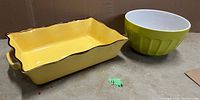 Two ceramic kitchen items: a yellow rectangular casserole dish with brown scalloped edges and a green mixing bowl with a white interior arranged side by side on a surface.