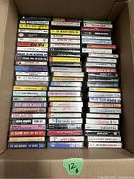 Boxed collection of 48 cassette tapes stacked upright with spine labels visible, showing various titles and artists from the 1980s.