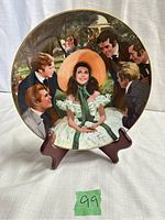 Front view of the Gone With The Wind collector plate titled 'Scarlett and Her Suitors' on a wooden holder.