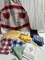 Overall photo showing the brand new Christmas apron and assortment of various tea towels and kitchen cloths in different colors and patterns, some with tags.