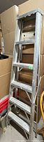 Aluminum step ladder positioned among stacked boxes and storage bins, showing overall condition and structure.