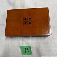 Closed wooden box with card suit symbols on the lid and magnetic closure, showing compact size with hand for scale.