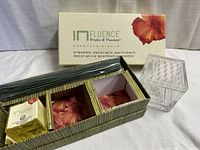 Photo of the reed diffuser set including unopened fragrance oil, square glass container with perforated lid, and reeds inside original packaging box labeled Influence by Fruits and Passion.