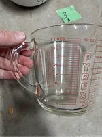 Clear Pyrex glass measuring cup with red measurement markings up to 4 cups/32 oz and D handle shown held in hand.