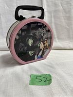 Front and side view of round metal lunchbox featuring The Wizard of Oz artwork with Wicked Witch and Dorothy, showing pink border and black handle