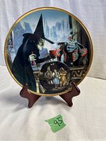 Full front view of the collector's plate on a wooden stand showing the Witch casting a spell scene including an inset with Dorothy, Scarecrow, and Tin Man.