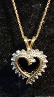 Front view of the heart-shaped pendant with diamonds on a gold necklace, shown on black background.