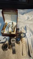 Full view of 8 watches including those in Lucien Piccard case and others laid out showing variety of bands and dials