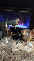 Wide view of the Fiberwe large mixer body, stainless steel bowl, and three mixing attachments arranged on carpeted floor in front of fireplace.