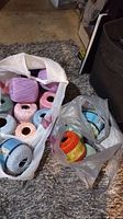 Two plastic bags filled with various colored skeins of knitting yarn including pink, lavender, peach, blue, mint green, orange, and white colors.