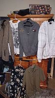 Photo showing a variety of men's XL clothing items including jackets, hoodies, and shirts hung on or positioned near a wooden dresser.