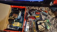 Wide angle photo of box containing multiple Micro Gauge trains, track pieces, and village buildings, showing variety and quantity of items included.
