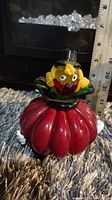 Side-front view of Murano glass potbelly clown figurine with facial details including yellow head, black top hat, red lips, and segmented red glass body shown next to a measuring tape about 6 inches tall.