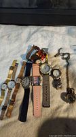 Full view of all seven watches and pocket watch with chain laid on towel surface.