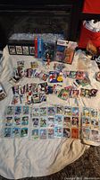 Wide shot showing an assortment of sports cards spread out on a surface, and several boxed sports figurines in original packaging in background.