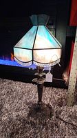 Front view of vintage sterling plated lamp with blue and white slag glass octagonal shade, showing size against ruler and visible shade damage.