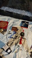 Overview of all items spread out on white cloth including various boxes, rosaries, necklaces with elephant pendant, compact, and hand-painted egg