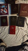 Seven vintage religious books including various editions of the Holy Bible and related texts, displayed on fabric surface.