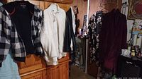 Photo of six women's clothing items hung on a wooden wardrobe including jackets, robes, and a shirt