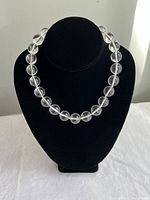 Front view of the clear acrylic bead necklace arranged on a black display bust on a white fabric background.