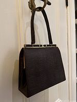 Side angle view of purse hanging, showing exterior shape and top handle