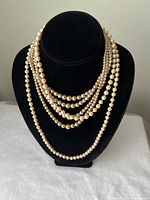 Multi-strand faux pearl necklace displayed on bust showing cream-colored varying size pearls in five strands.