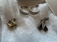 All three pairs of earrings on white textured padding showing the silver hoops, black onyx with marcasite drops, and tear drop stud earrings.