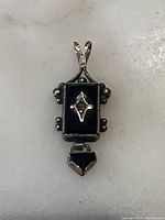 Frontal view of rectangular onyx pendant with central gold motif and triangular onyx drop