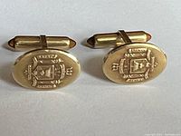 Front view of the gold-tone oval Naval Academy cufflinks showing embossed crest detail.