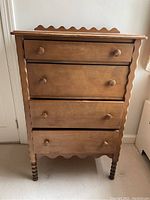 Front view of antique hardwood dresser showing four drawers, scalloped gingerbread style edges, and turned legs.